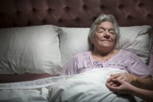 Young woman holding sleeping senior woman's hand