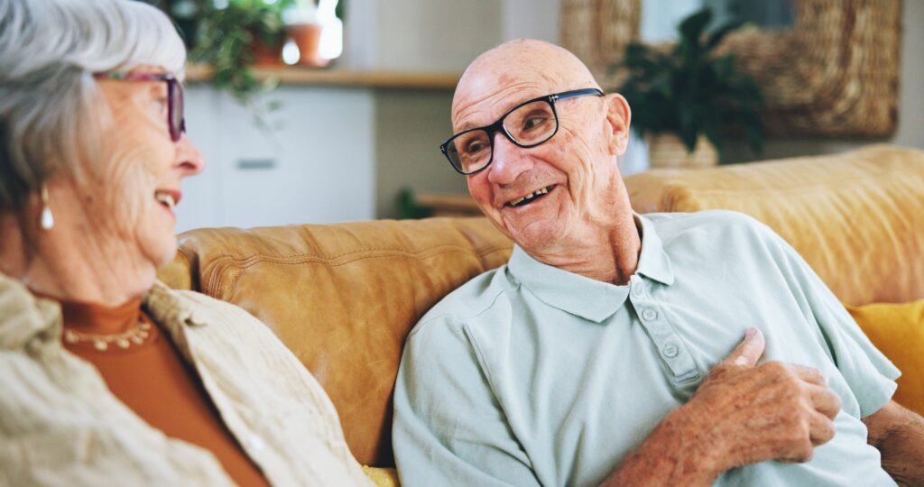 Senior couple, talking and happy on sofa with memory, care and bonding with love in home living roo